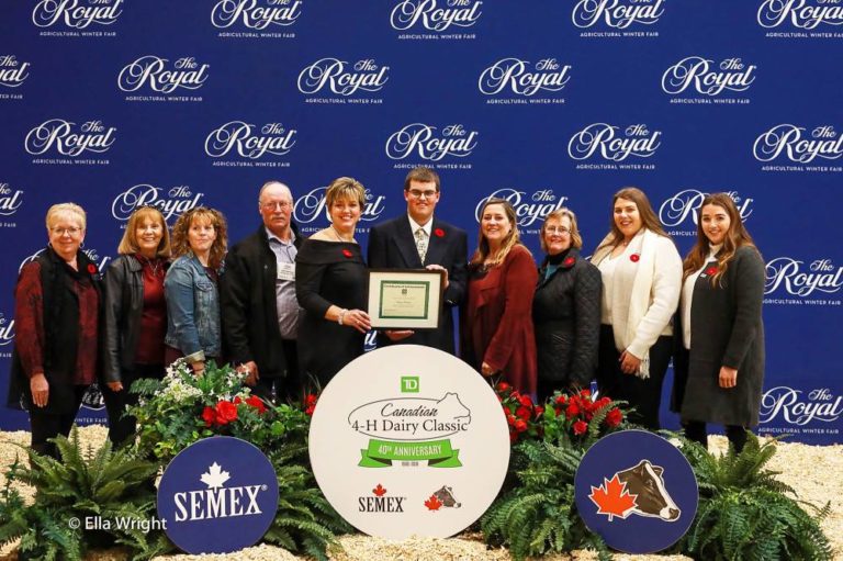 Scholarship recipient standing infront of blue backdrop and other volunteers at the Royal Agricultural Winter Fair