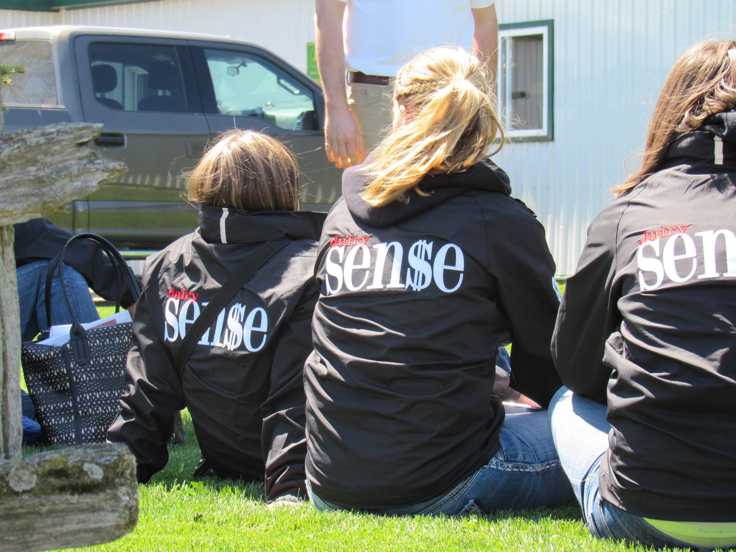 Kids sitting on grass in front of barn wearing Dairy Sense conference jackets